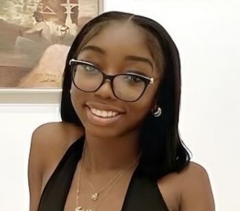 Smiling student with long black hair and a black top, wearing glasses.